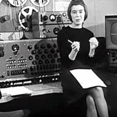 Delia Derbyshire seated among tape machines and oscillators at the BBC Radiophonic Workshop