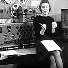Delia Derbyshire seated among tape machines and oscillators at the BBC Radiophonic Workshop