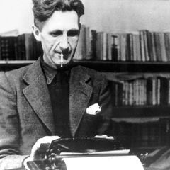 George Orwell typing at a desk, bookshelves behind him