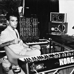 Nuno Canavarro seated beside a modular synthesizer and Korg keyboard in a home studio