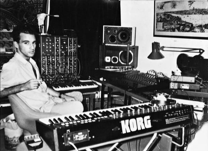Nuno Canavarro seated beside a modular synthesizer and Korg keyboard in a home studio