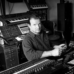 Pete Namlook seated among racks of synthesizers and keyboards in his studio
