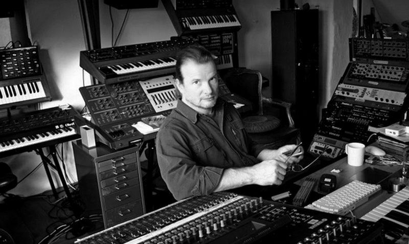 Pete Namlook seated among racks of synthesizers and keyboards in his studio