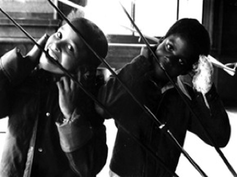 Two children listening to a Rainforest sculpture through long rods held to their ears