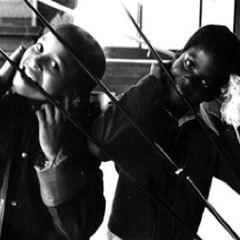 Two children listening to a Rainforest sculpture through long rods held to their ears