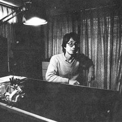 Satoshi Ashikawa seated at a keyboard in a curtained studio