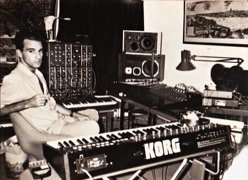 Nuno Canavarro seated beside a modular synthesizer and Korg keyboard in a home studio