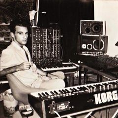 Nuno Canavarro seated beside a modular synthesizer and Korg keyboard in a home studio