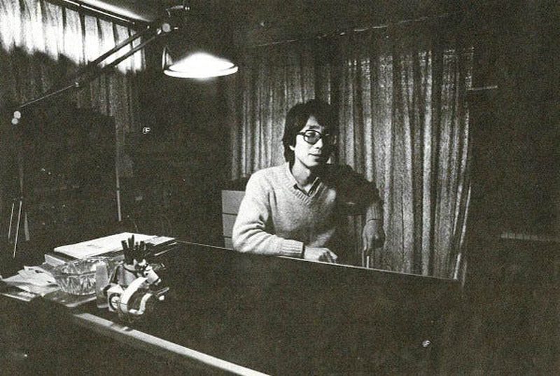Satoshi Ashikawa seated at a keyboard in a curtained studio