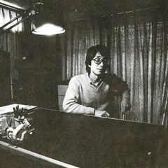 Satoshi Ashikawa seated at a keyboard in a curtained studio